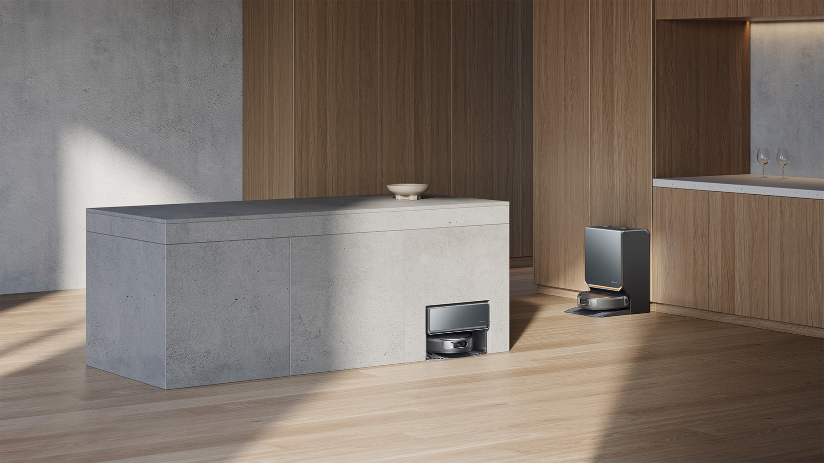 Two black robot vacuums in a kitchen, one under a concrete island, the second on its base