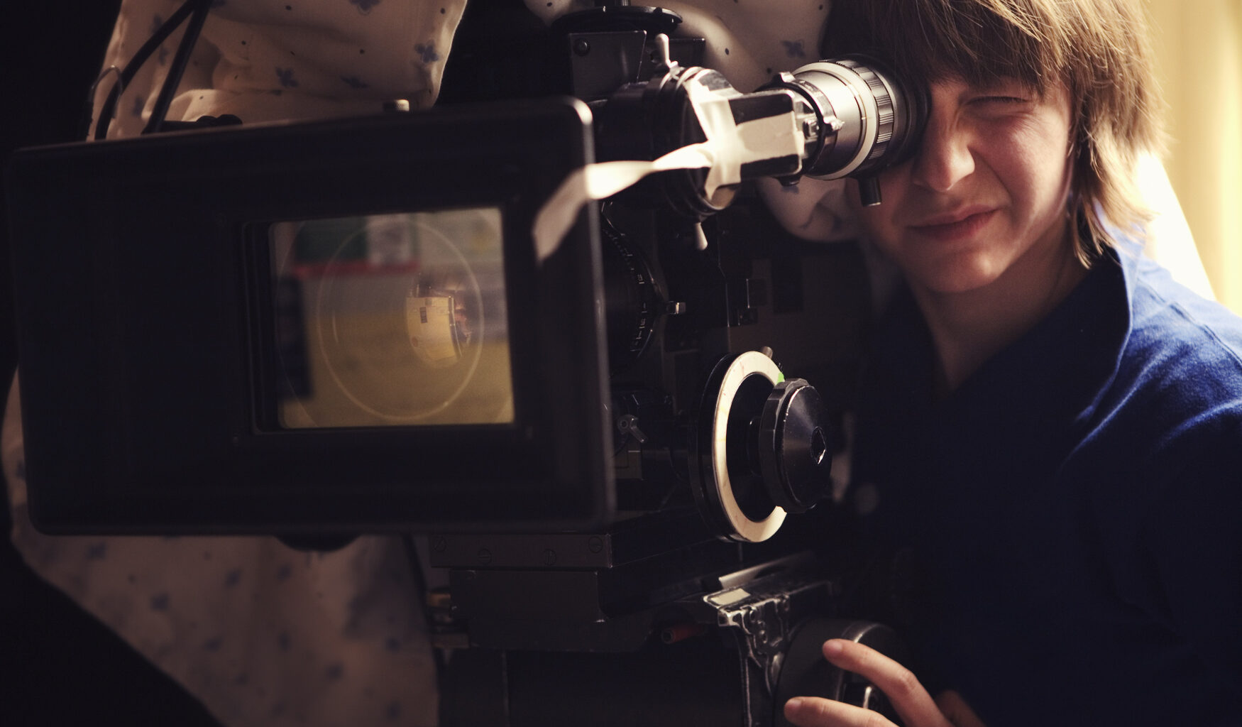 "A young woman operating a 35mm film camera. There is a blanket thrown over the camera to dampen the sound of the film running through it so it doesn't interfere with the scene.Shot on a real set at high iso, some noise, view at 100%.More filmmaking images:"