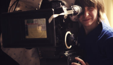 "A young woman operating a 35mm film camera. There is a blanket thrown over the camera to dampen the sound of the film running through it so it doesn't interfere with the scene.Shot on a real set at high iso, some noise, view at 100%.More filmmaking images:"