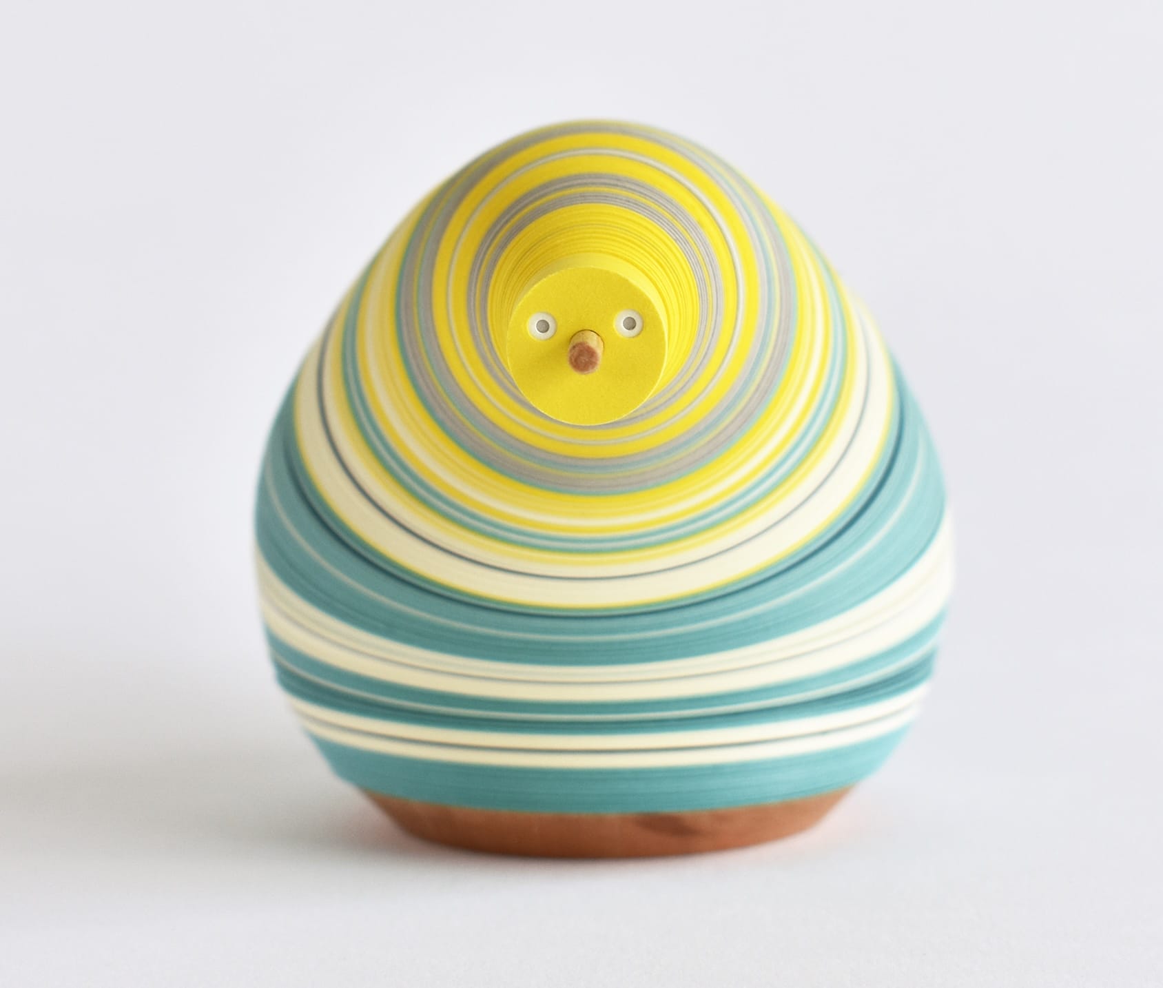 a small paper figure made from numerous layers of colored paper on a flexible central axis so that it looks like an anthropomorphized pear