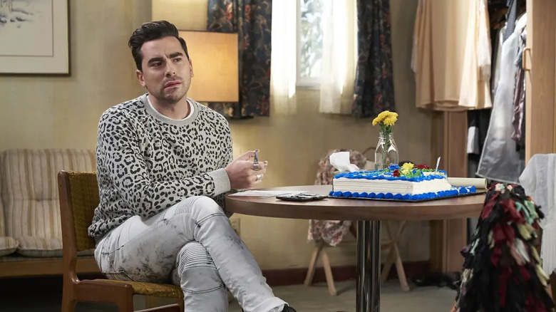 Dan Levy as David Rose sits at a table in Schitt's Creek