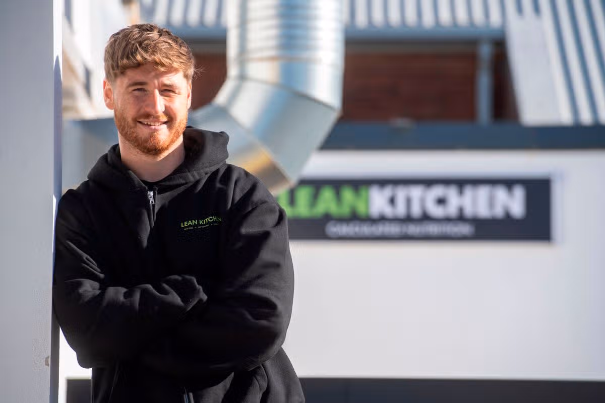 A man with a beard and black coat in front of a food van