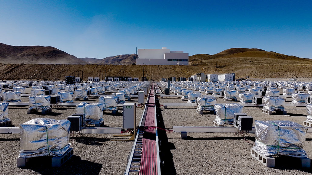 a photo of a wide gravel field with many silver fabric covered cube shaped packs of batteries on cement blocks