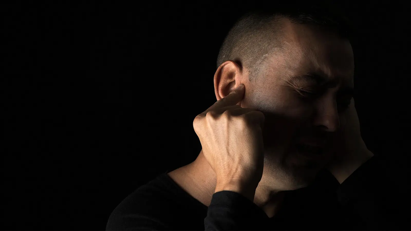 A photo of a man wincing and plugging his ears.