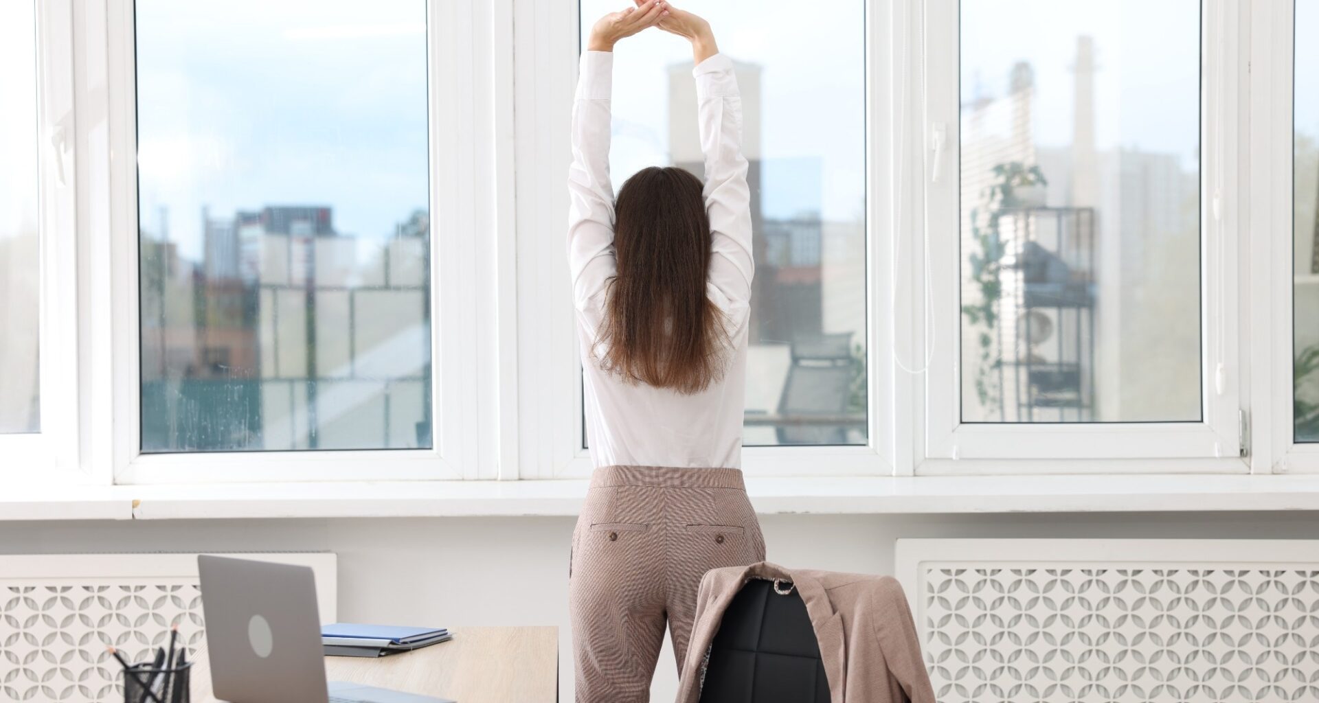 Young businesswoman doing stretching exercise in office, back view