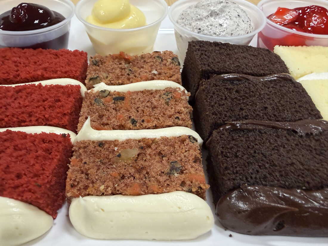 In the foreground is a row of wedding cake samples at a Publix supermarket in Vestavia Hills, Alabama, on September 23. The cake flavors from left to right are red velvet, carrot cake, chocolate and vanilla. In the background is a row of four small plastic cups, each with a filling in it. The filling flavors from left to right are raspberry, vanilla custard, cookies-and-cream mousse and strawberry.