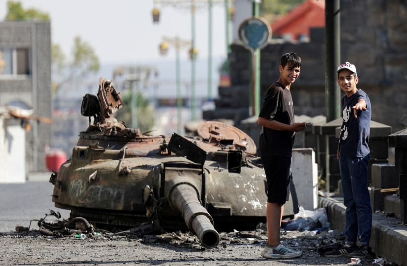 People stand next to a destroyed tank turret, following deadly clashes between Druze fighters, Sunni Bedouin tribes and government forces, in Syria's predominantly Druze city of Sweida, Syria July 25, 2025.