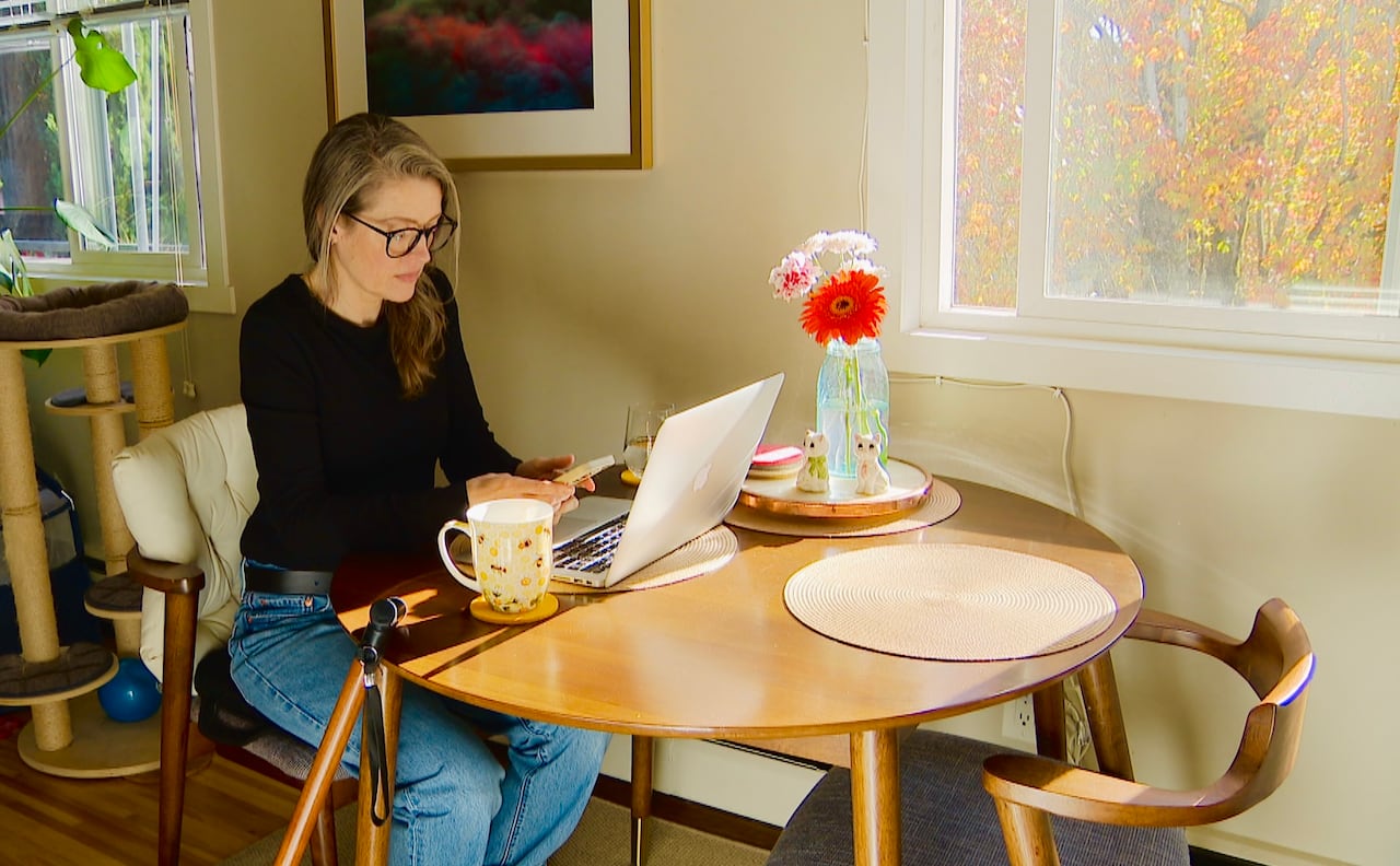 A woman sitting at a table in her apartment, typing on a laptpop.