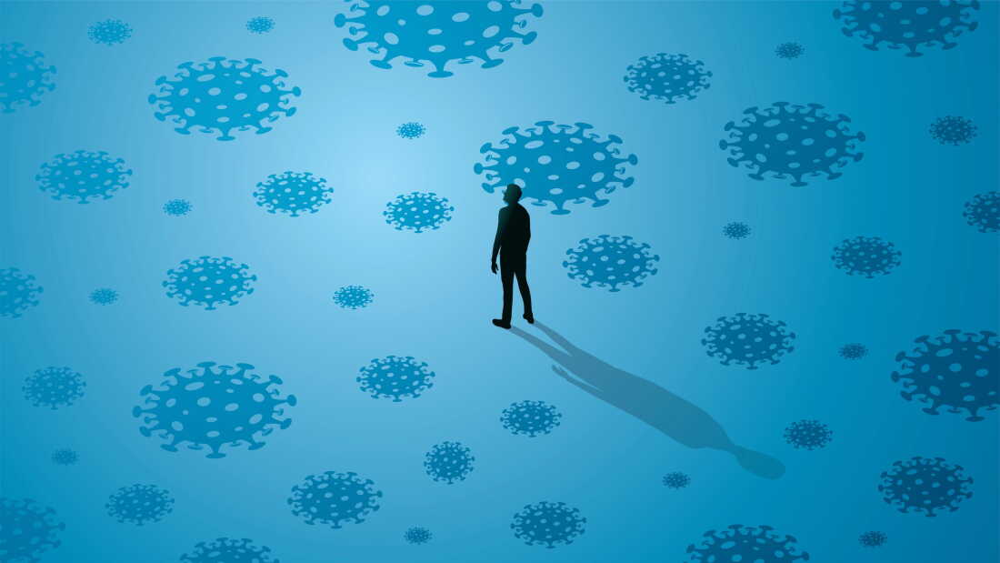 Abstract covid viruses surround the silhouette of a man standing alone against a blue background.