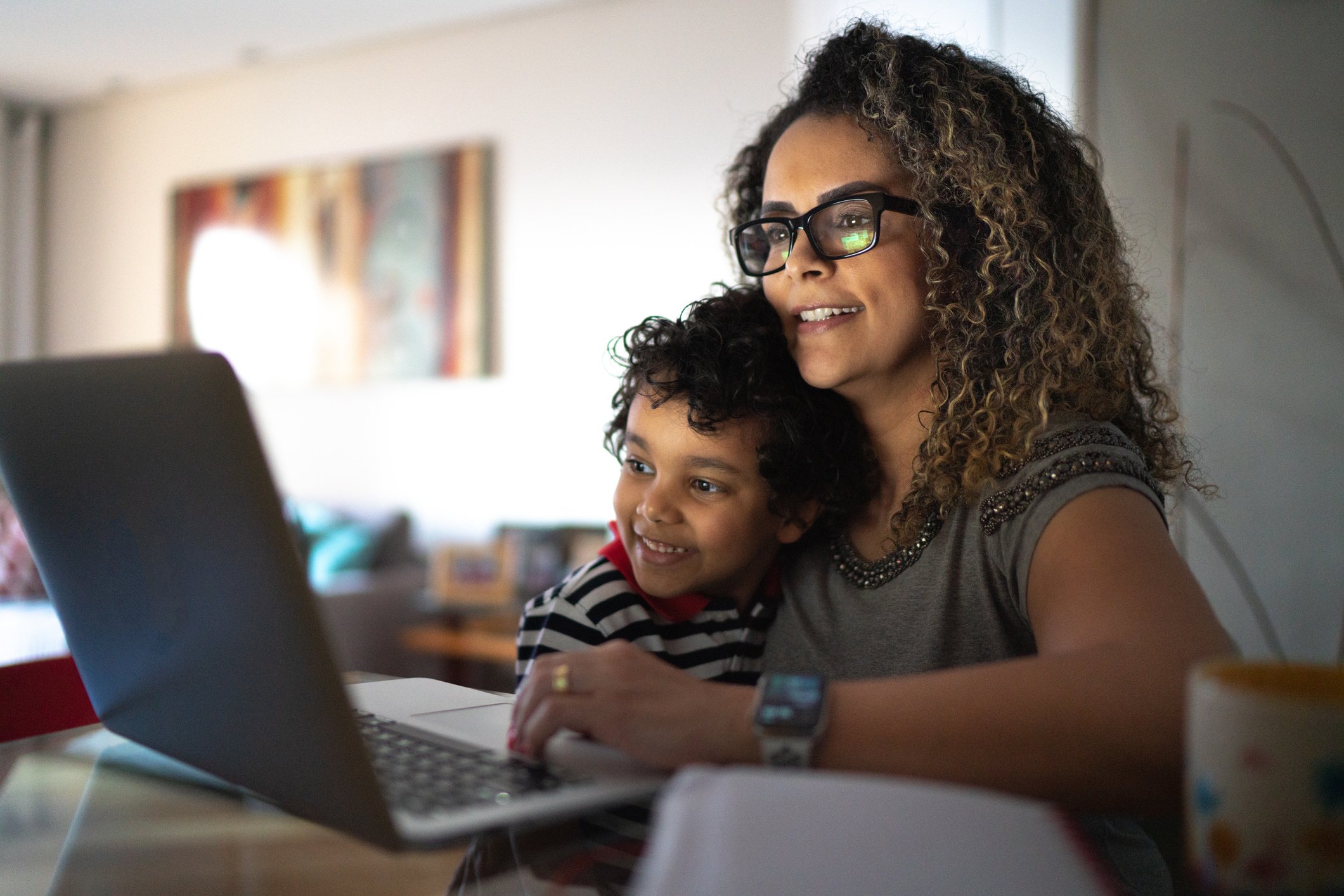 Parent hugging child and looking at laptop.
