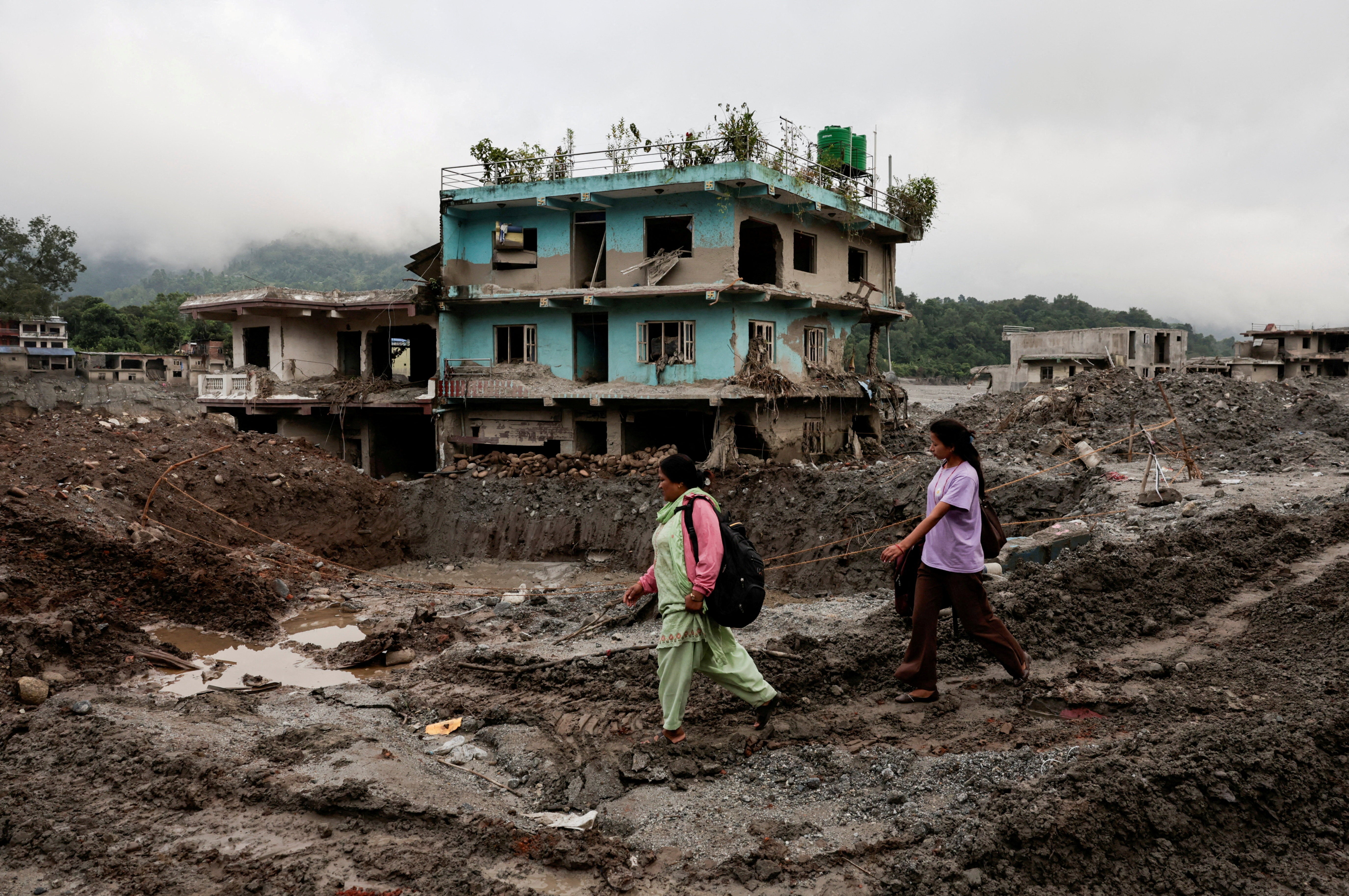 People walk past damaged houses following deadly flash floods and a mudslide in Devighat, Nuwakot district, Nepal
