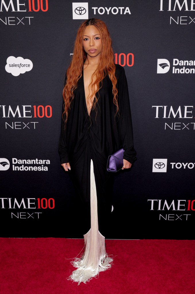 Ravyn Lenae attends the TIME100 Next Gala in a black gown with a plunging neckline and white fringed detailing at the hem, holding a purple clutch.