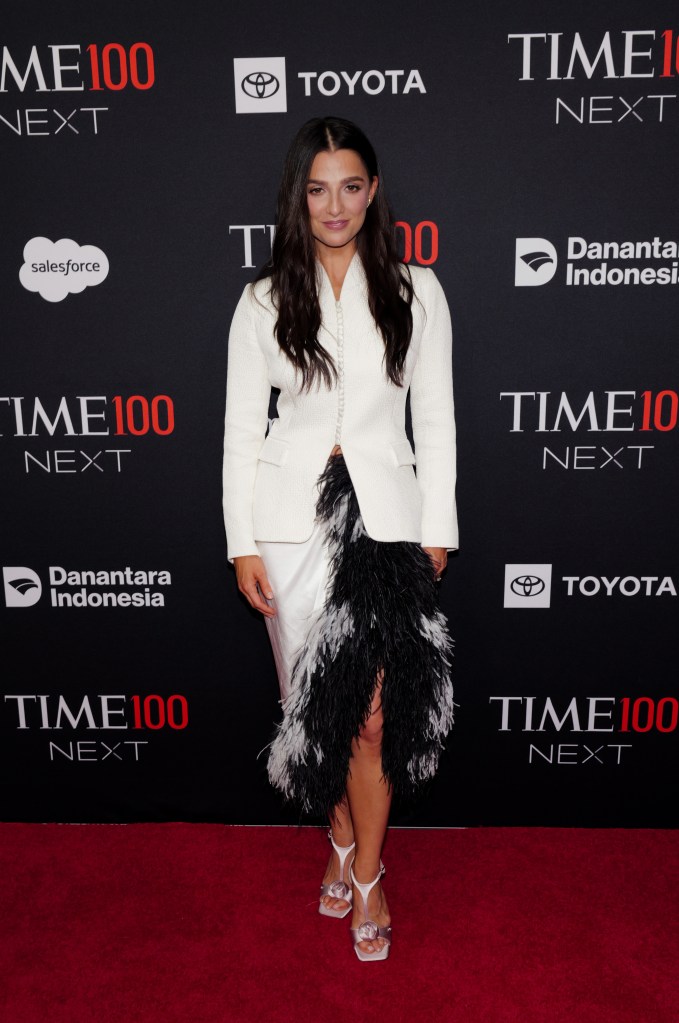 Marisa Abela poses on the red carpet at the TIME100 Next Gala wearing a white jacket and a white skirt accented with black and white feathers.