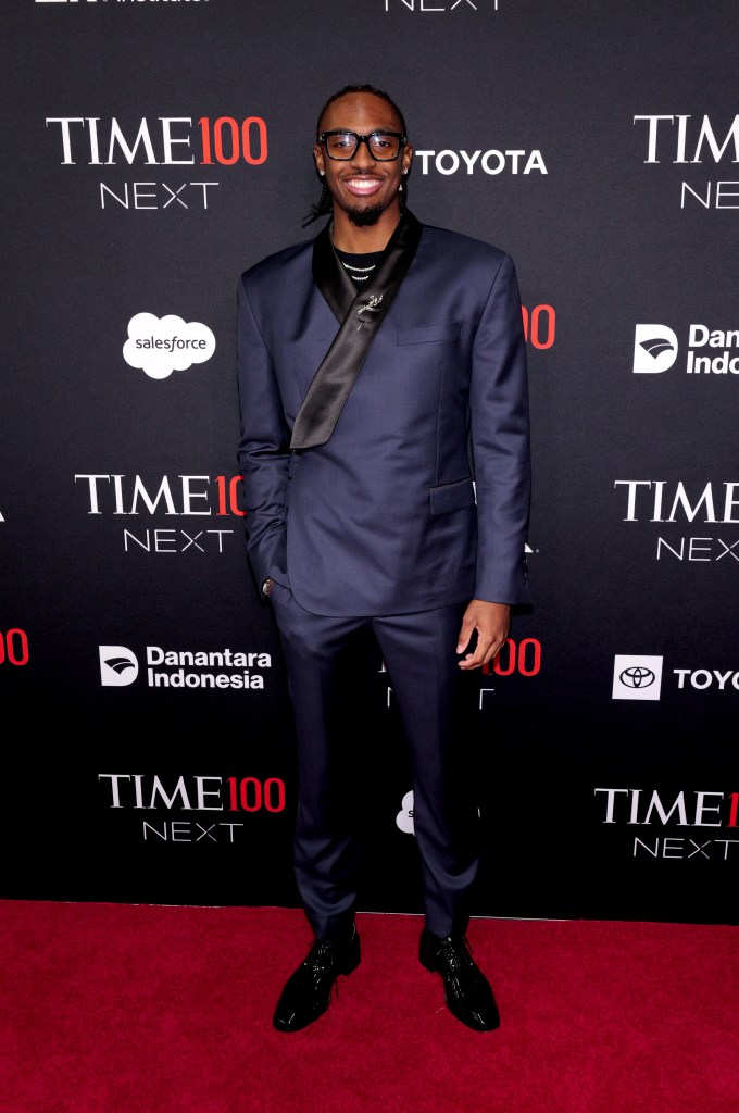 Tyrese Maxey attends the TIME100 Next Gala in a dark suit with a satin lapel, wearing glasses.
