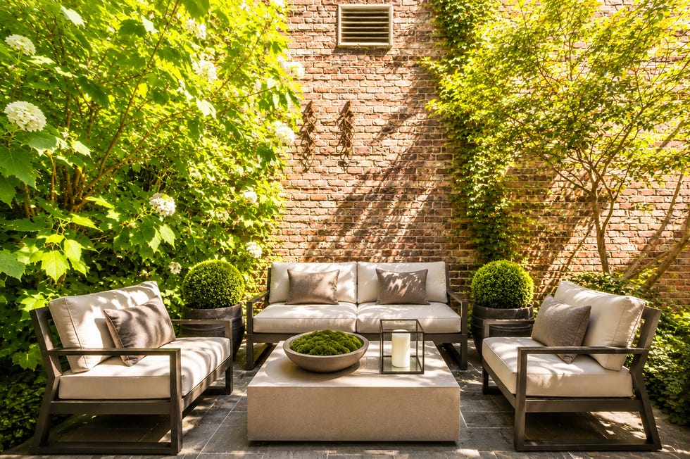 Cozy outdoor seating area with plush furniture surrounded by lush greenery and a brick wall.