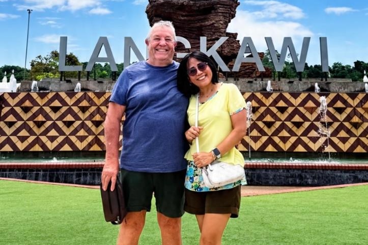 Robert Donnelly and a woman stand in front of Langkawi sign.