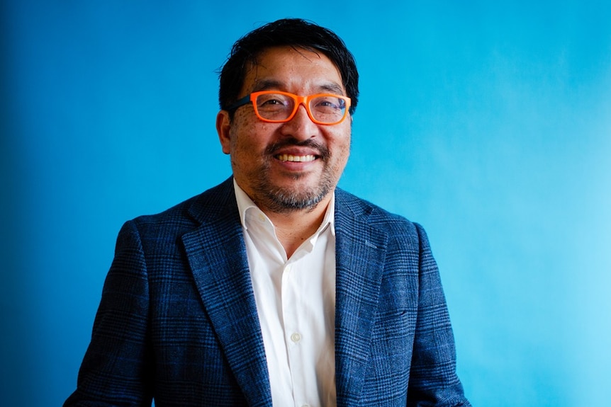 A corporate headshot of John Chan in orange glasses.