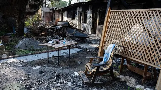 The burnt exterior of a house with a charred rocking chair and table, an Israeli flag laid over