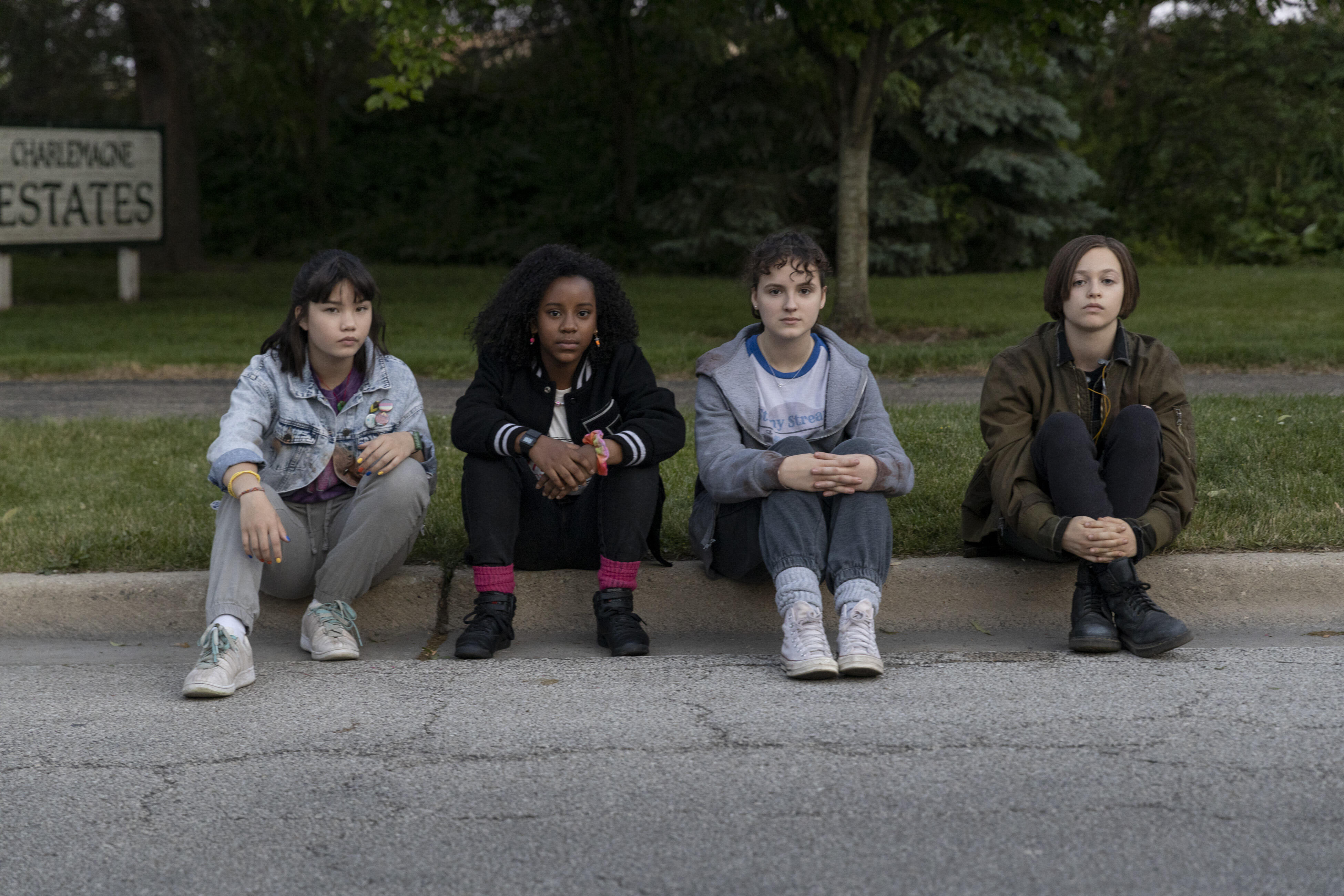 Four teenage girls sit on the curb.