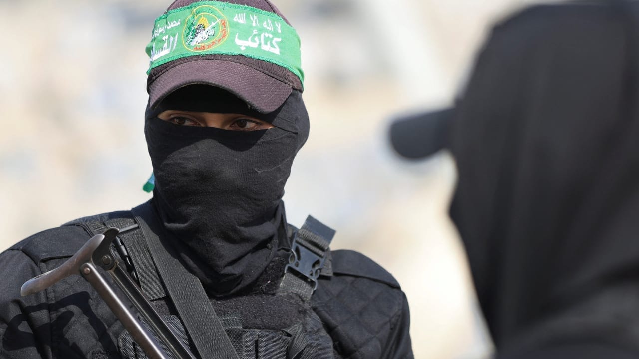 Hamas members look on as they escort members of the Red Cross towards an area within the yellow line, in Gaza City, November 12, 2025.  