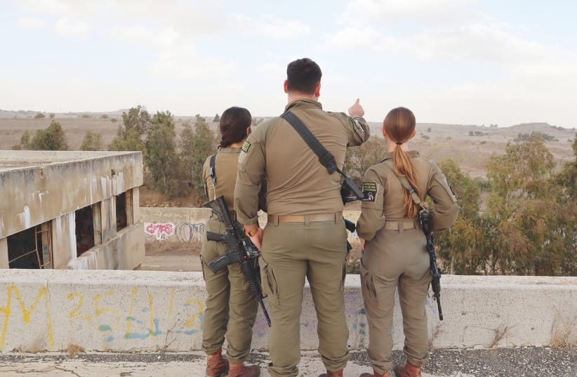 Capt. 'O.', commander of a field intelligence company in Battalion 595, points towards Syrian territory alongside female intelligence collection soldiers 'N.'' and 'R.' The unit conducts surveillance operations across southern Syria to identify potential threats to Israel.