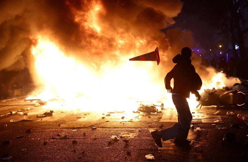 A man throws a plastic traffic cone through a burning barricade amid clashes during a day of demonstrations, France, October 17, 2026