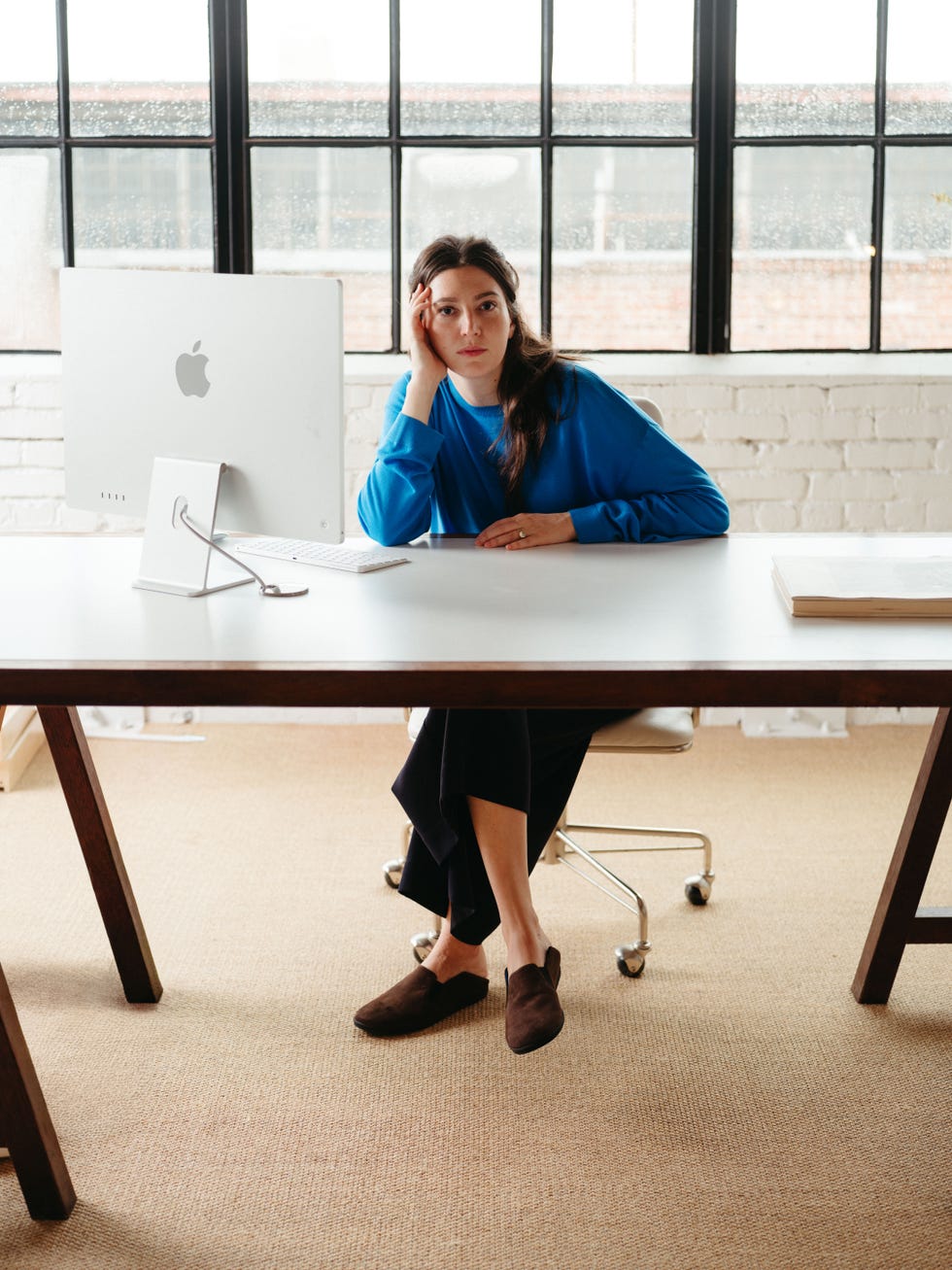 Young woman sitting at a desk with an Apple computer, looking thoughtfully while resting her hand on her face.