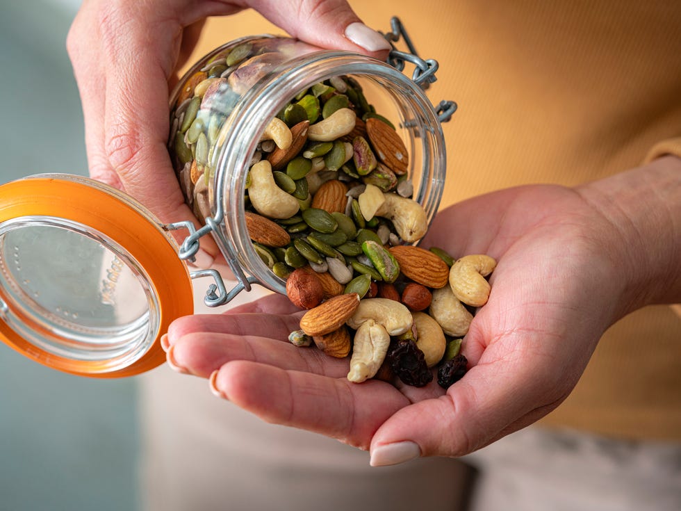 Close up of woman's hands spilling out nuts and seeds from container to the the palm of hand close up of womans hands spilling out nuts and seeds from container to the the palm of hand