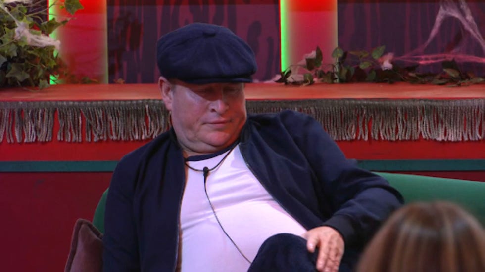 big brother philip person wearing a flat cap sitting on a couch in a decorated room.