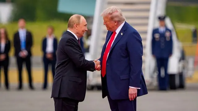 Putin and Trump dey shake hands, wit Air Force One for di background.