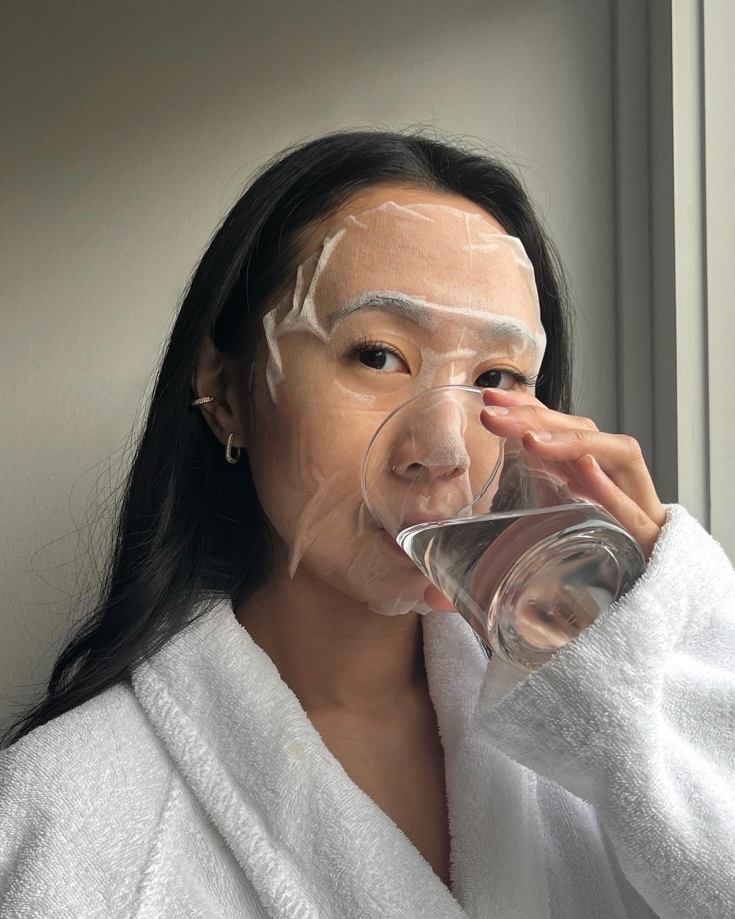 A woman drinking a glass of water with a face mask on