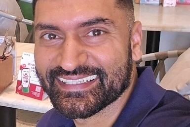 Amlan Sharma smiles widely in a selfie at a resteraunt.