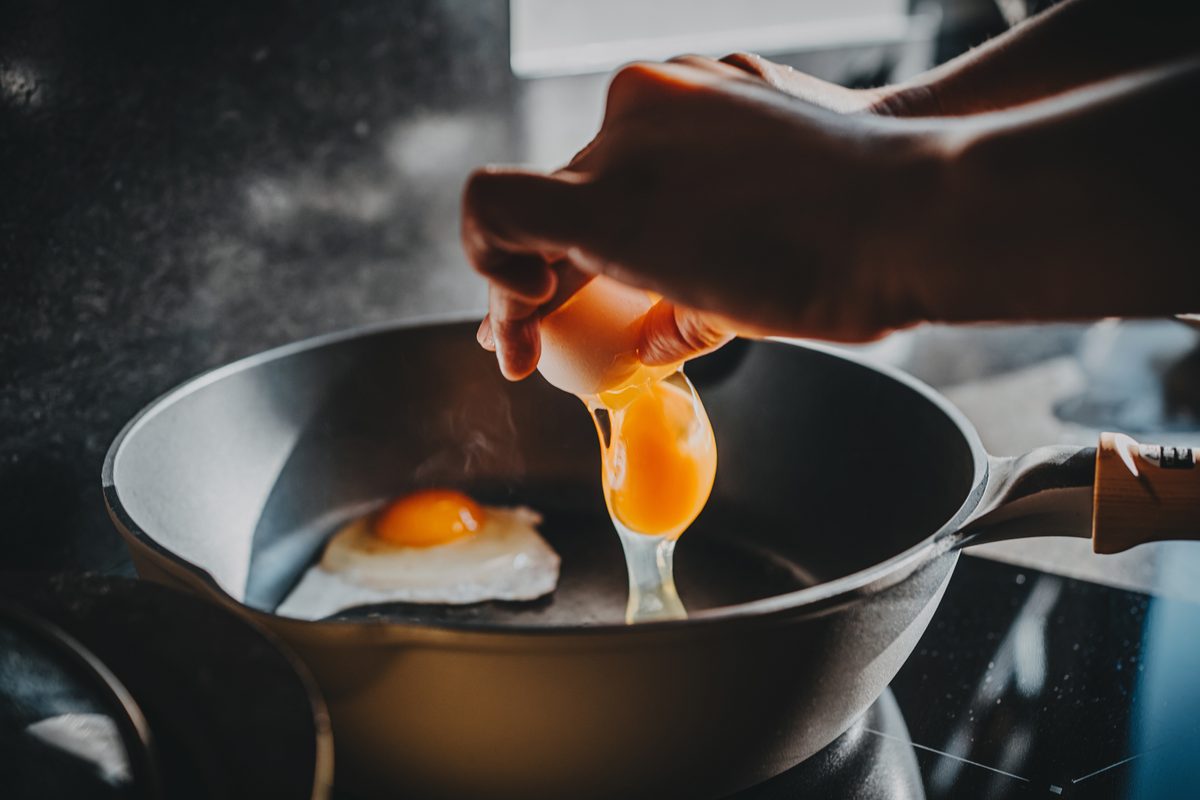 Close-up of female hand cracking an egg into a sizzling hot frying pan