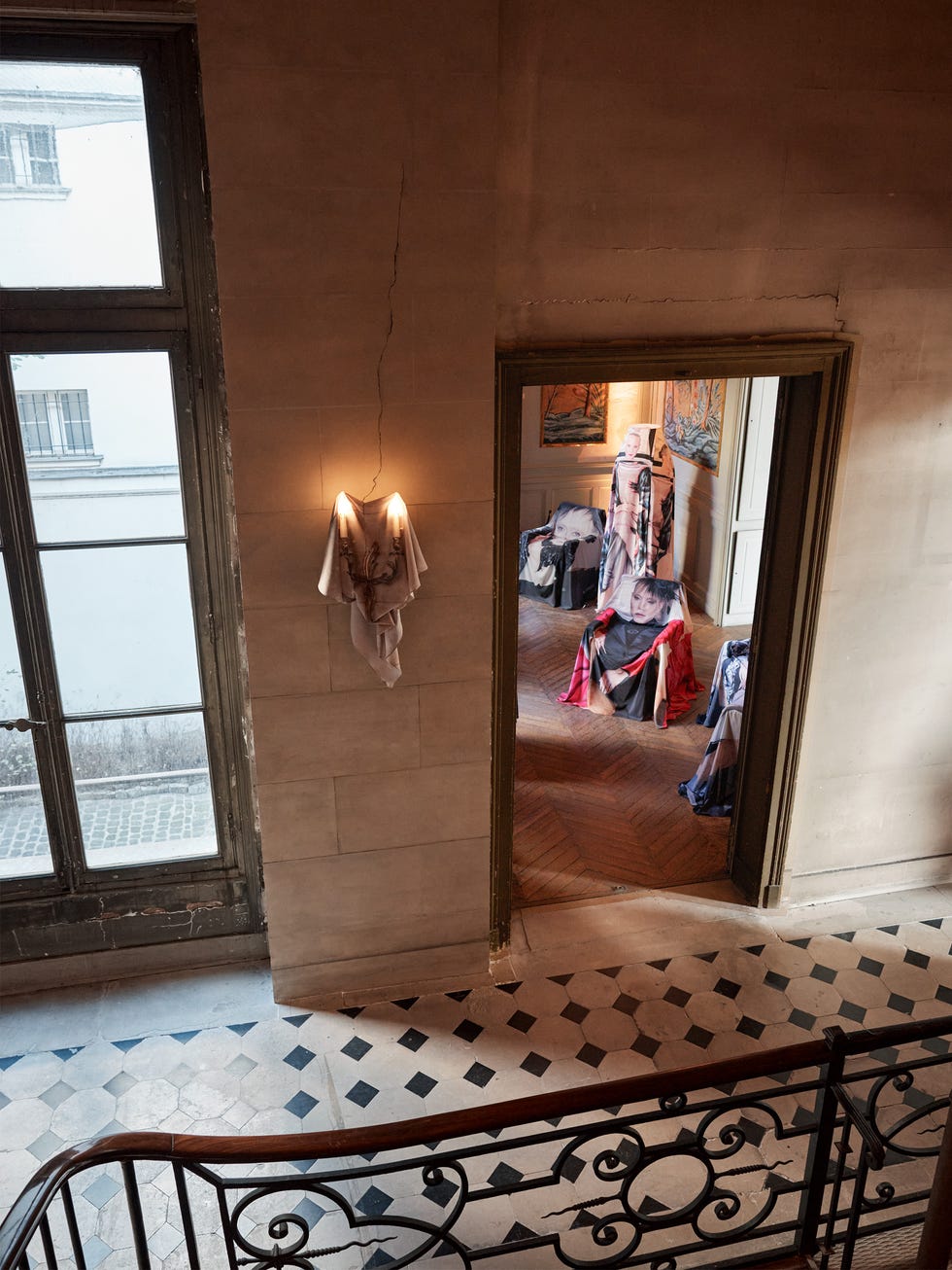 An interior view showing a hallway with art displays and patterned flooring, illuminated by a wall light.