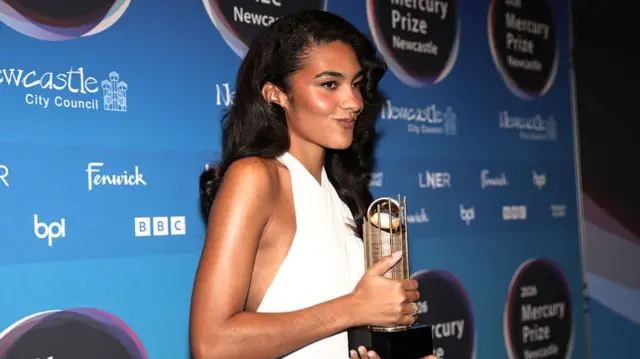 Olivia Dean poses in a white dress on the red carpet
