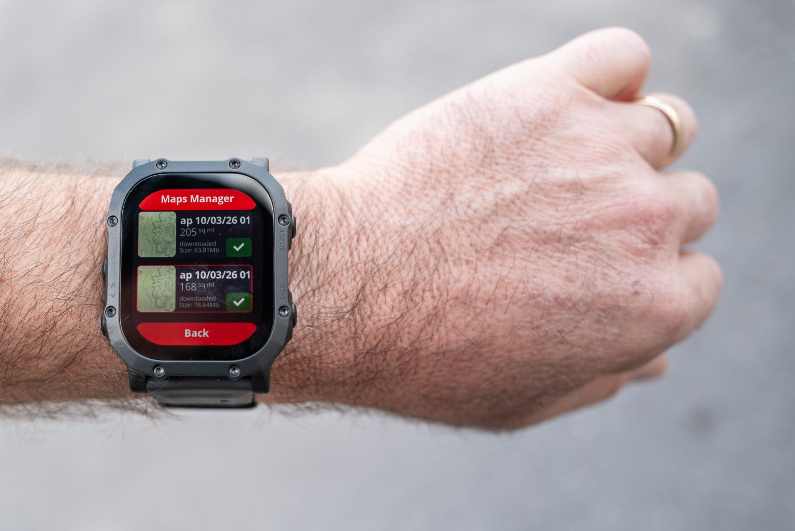 Bridger Reckon rugged smartwatch with a square black case on a wrist, its screen showing a red and black Maps Manager menu with two downloaded offline maps.