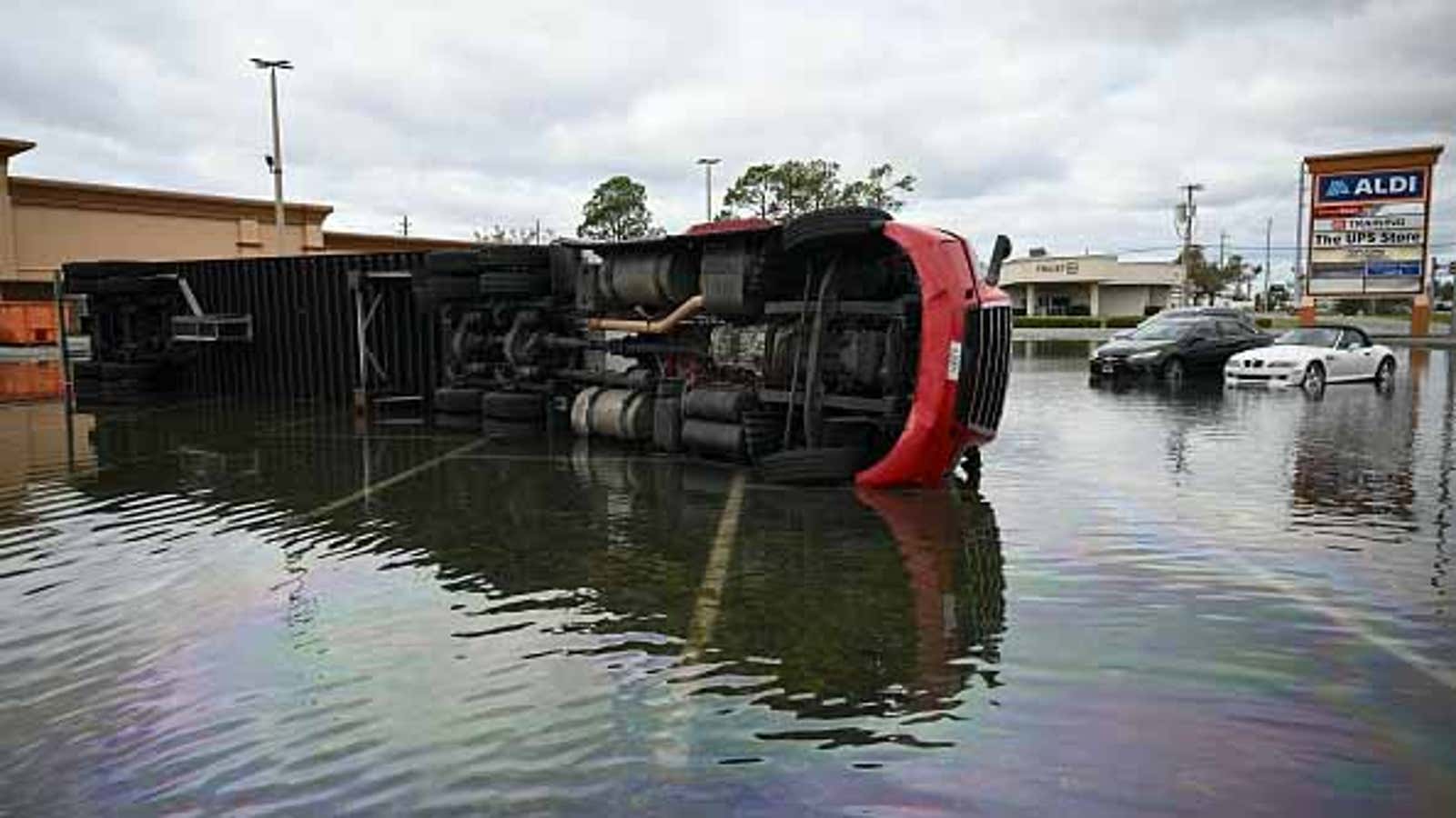 Overturned semi-truck and submerged cars in flooded parking lot near Aldi store.