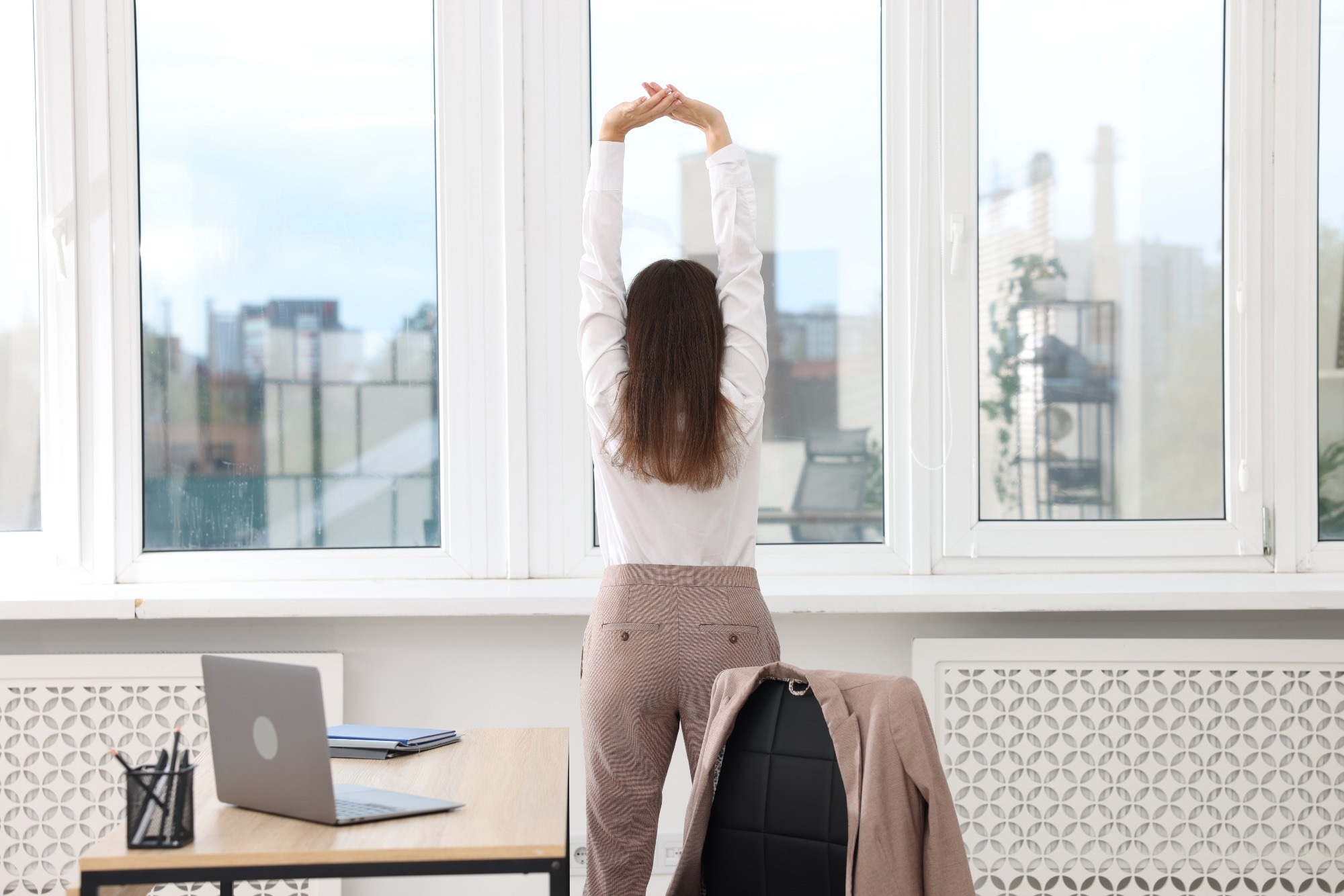 Young businesswoman doing stretching exercise in office, back view