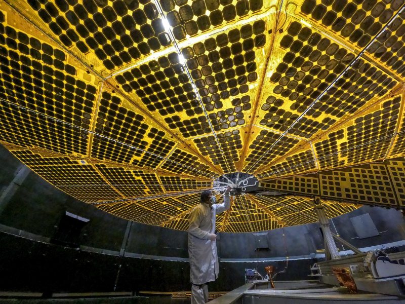 Large solar array with man in white protective suit standing under it.
