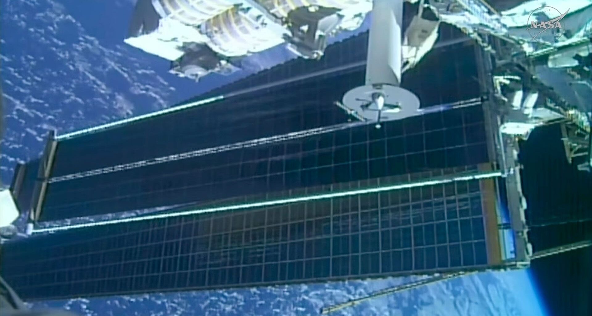 a view of two solar array panels, one overlapping the other, extending from a space station while in orbit over a blue planet