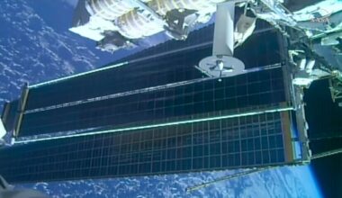 a view of two solar array panels, one overlapping the other, extending from a space station while in orbit over a blue planet