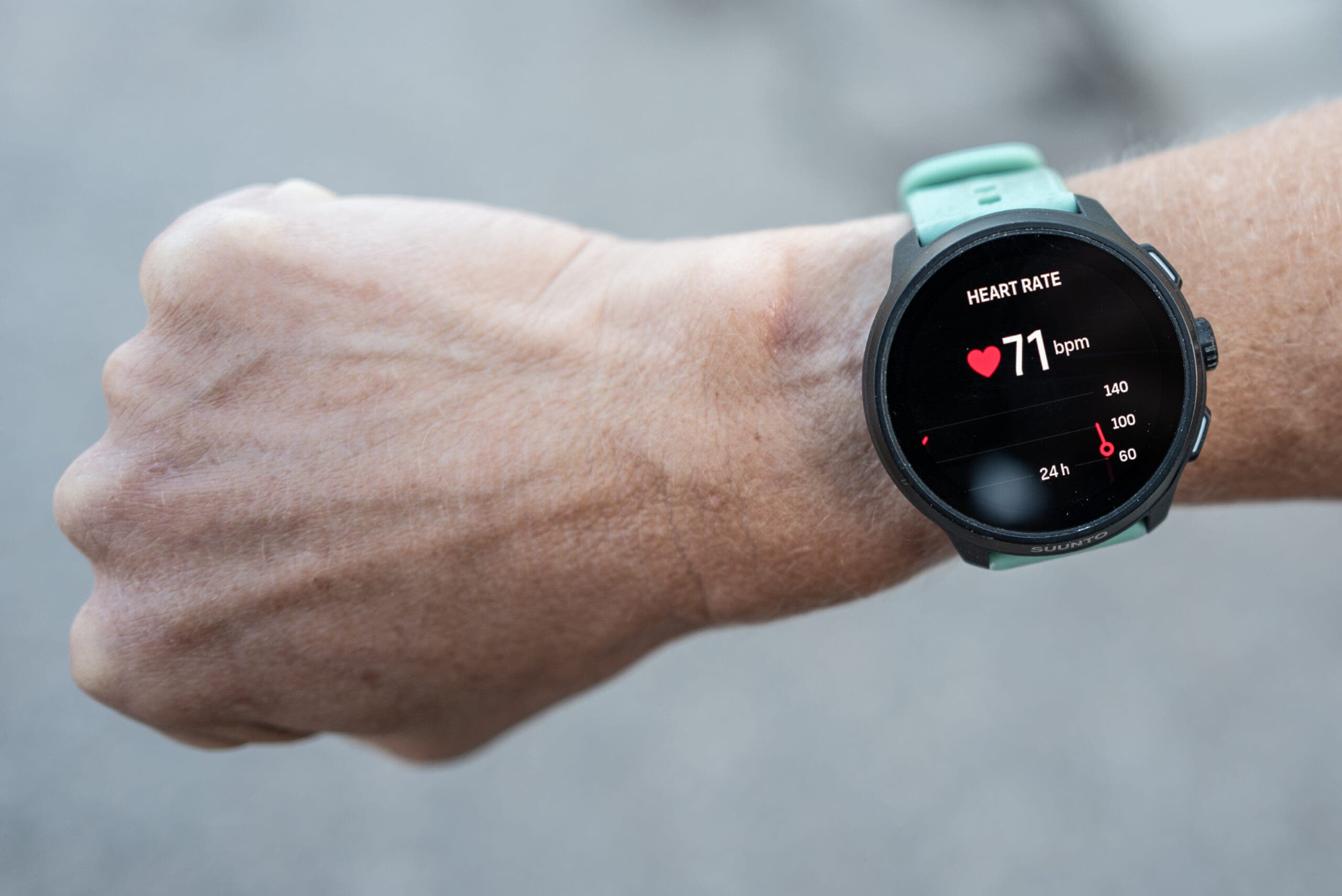 Suunto Run 2 watch with a mint green silicone strap on a wrist, its black screen showing a heart rate of 71 bpm and a heart rate graph.