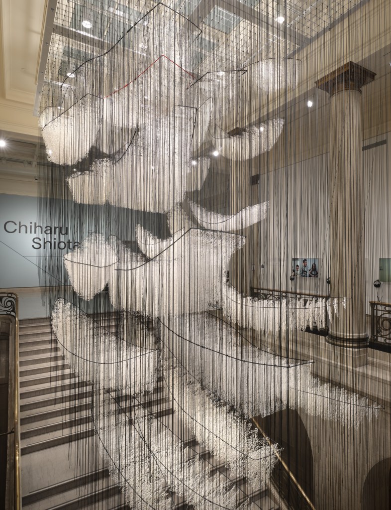 A grand staircase at MMFA with white ship-like shapes hanging above the step by black threads.