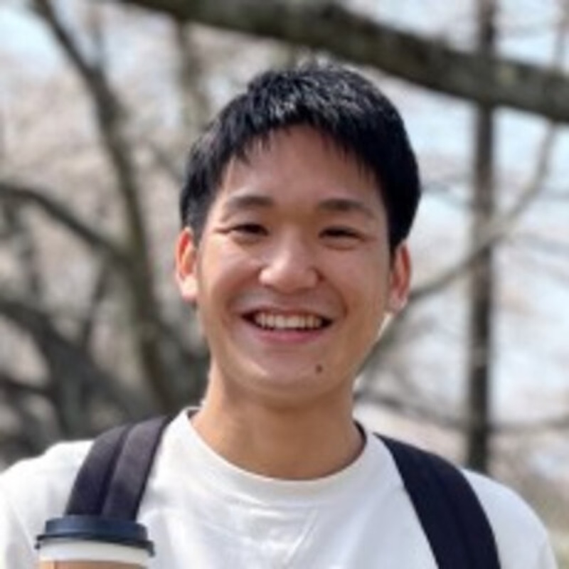 Smiling Asian man wearing a white t-shirt and backpack.