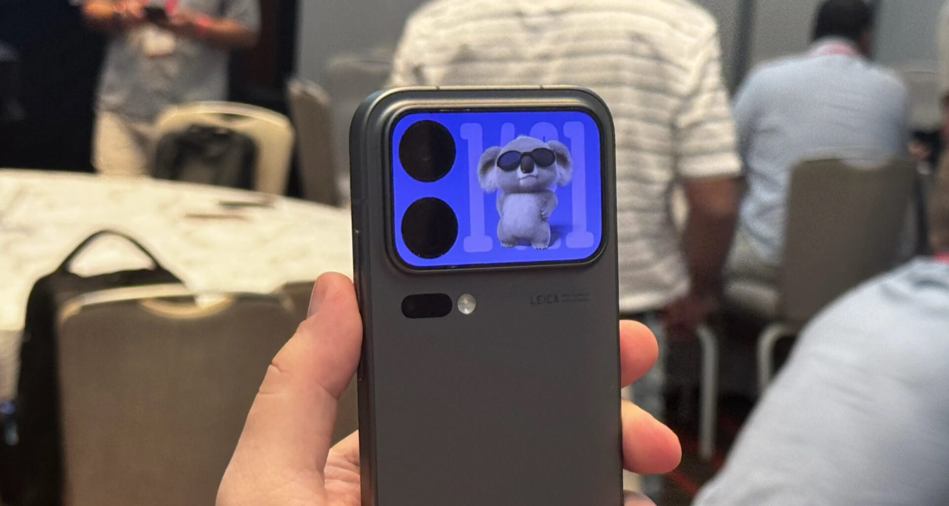 A hand holds up the back of a phone showing a rear screen with a koala bear animation.