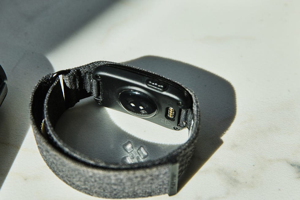 Wristband device with USB-C port and metal connectors, shown on a light surface with shadows.