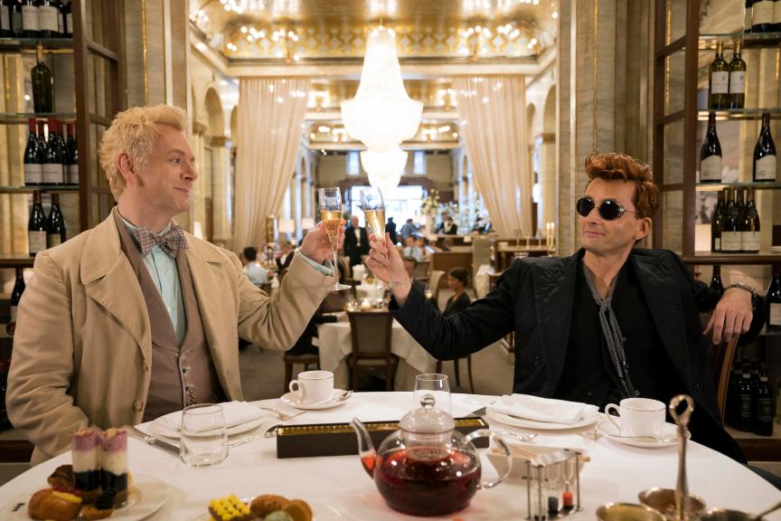 Michael Sheen and David Tennant clink glasses of champagne in production still from Good Omens.