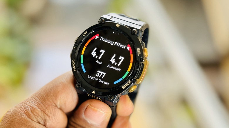A hand holding an Amazfit T-Rex smartwatch, the watch is displaying workout information