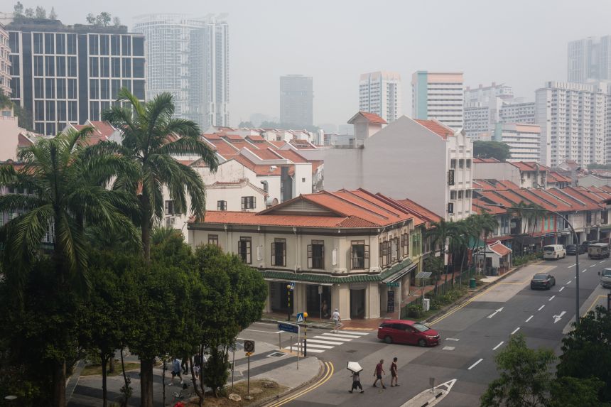 Pedestrians walk across a road as buildings are seen shrouded by haze in Singapore on October 9, 2026. Indonesia has been battling fires for weeks in parts of Borneo and Sumatra, sending suffocating haze across the islands and neighbouring Malaysia and Singapore.
