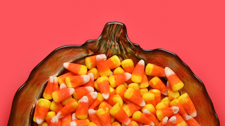 Candy corn in a pumpkin dish on a salmon pink background.